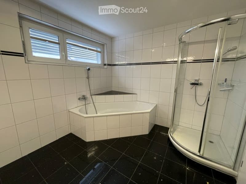 Modern bathroom with white tiled walls, black tiled floor, corner bathtub, and a glass-enclosed shower stall.