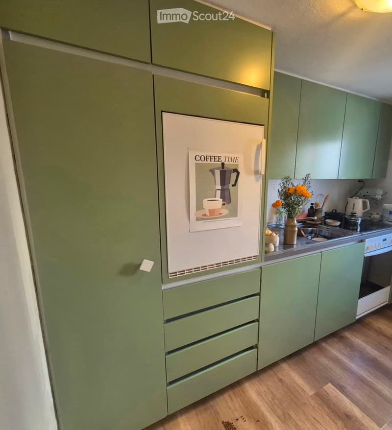 Modern kitchen with green cabinets, a refrigerator with a 'COFFEE TIME' poster, a sink, stove, and various kitchen items on the counter.