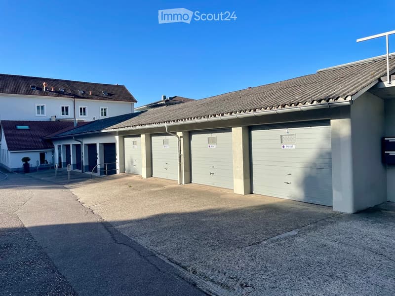 A multi-unit residential building with a large garage area, featuring multiple garage doors and a paved driveway.