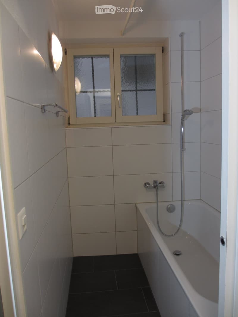 Bathroom with white tiles, bathtub, shower, window, and a light fixture.