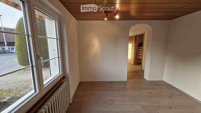 Empty hallway with wooden flooring, white walls, large windows, and a staircase leading upwards.