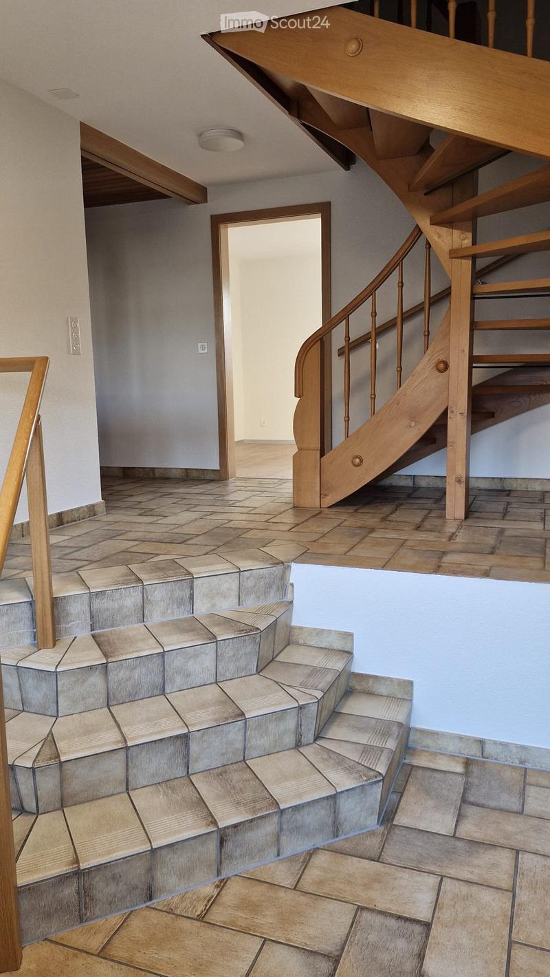 Spacious hallway with a wooden staircase leading to an upper level, featuring geometric tiled steps and a wooden handrail.