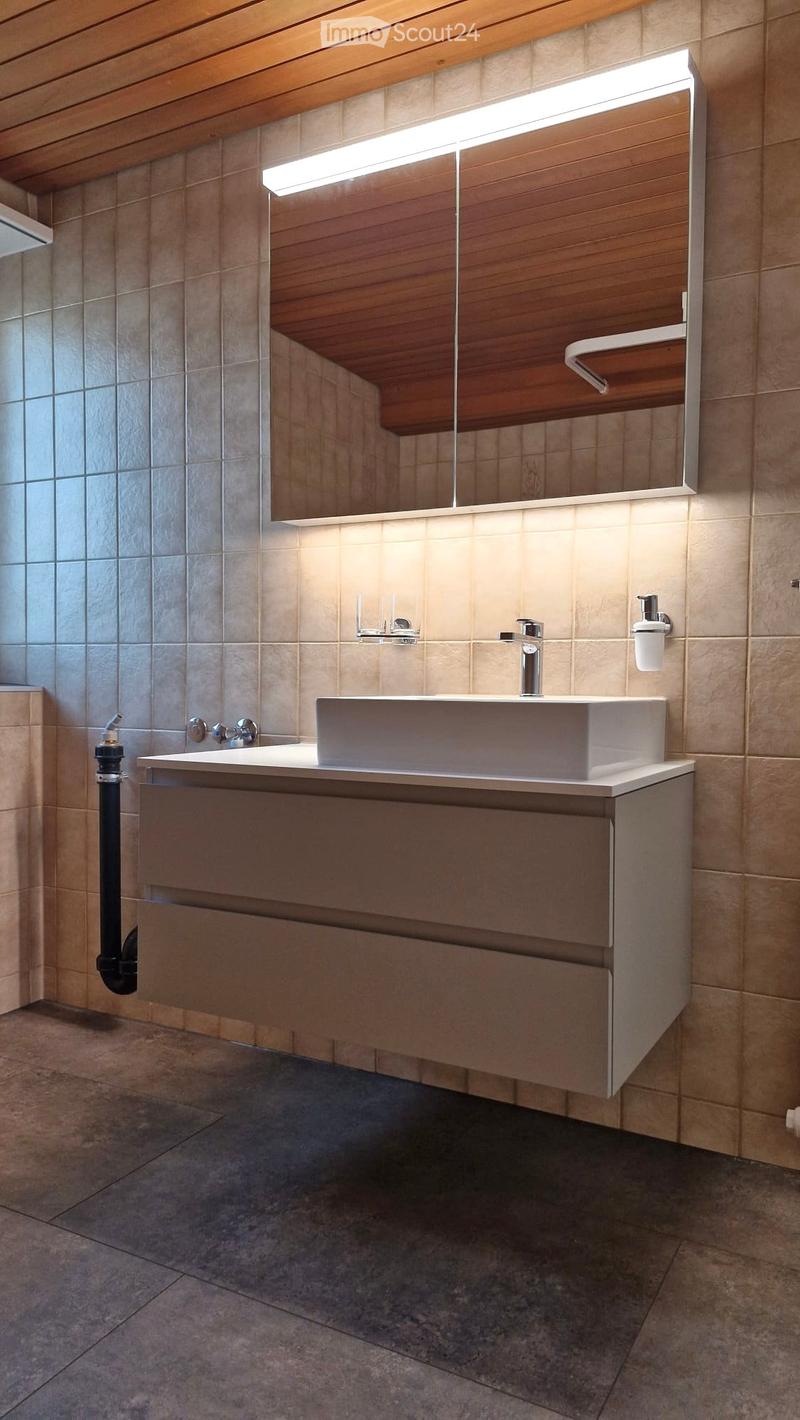 Modern bathroom with a white sink, sleek faucet, large mirror with wooden frame, and built-in cabinet.