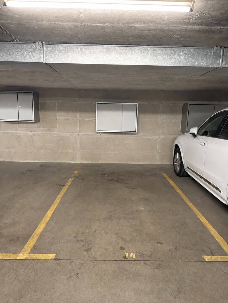 Underground parking space with concrete walls, yellow parking lines, and a white car parked in one of the designated spots.