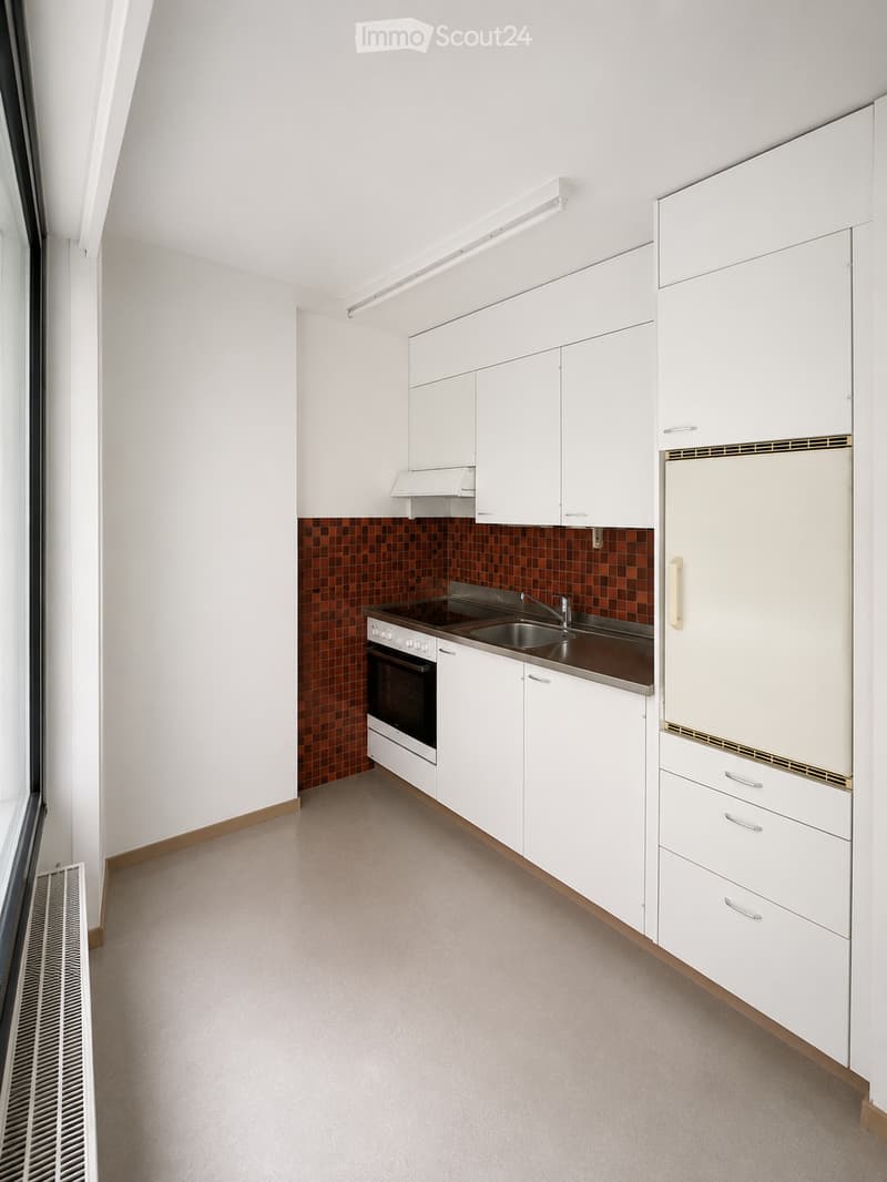 Modern kitchen with white cabinets, stainless steel appliances, and a dark brown countertop. Features an oven, sink, and refrigerator.