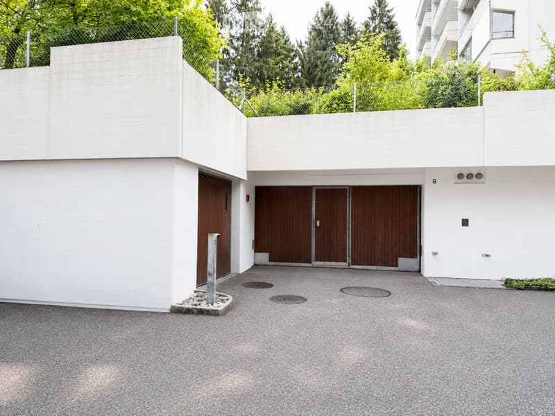 Modern two-story building with a white facade, large wooden garage doors, and a paved driveway.