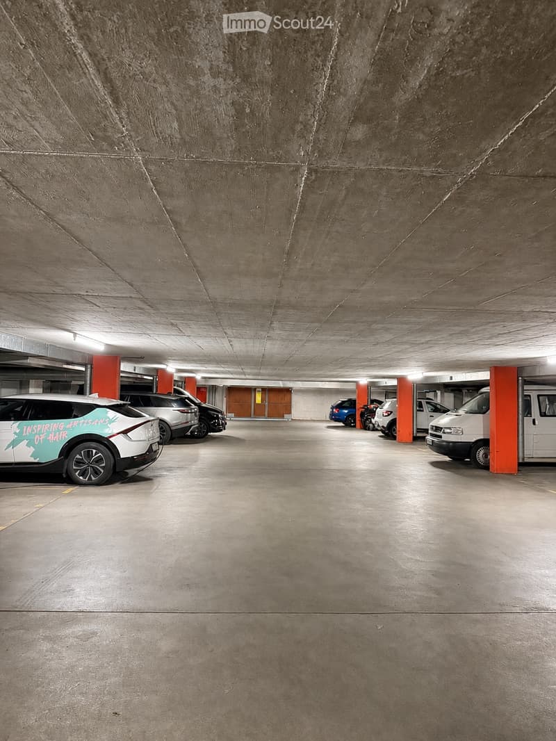 Underground parking area with several parked cars, concrete pillars, and a concrete ceiling.