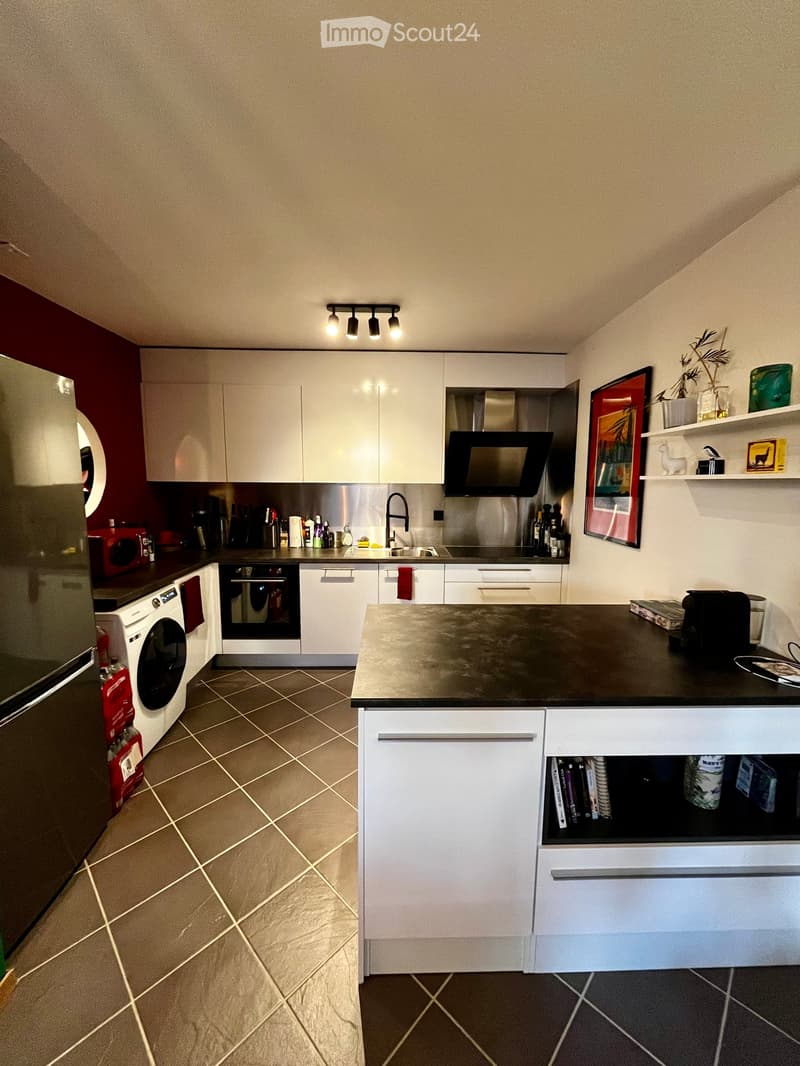 Kitchen. Modern kitchen with white cabinets, stainless steel appliances, and a black countertop island. Features include a refrigerator, oven, microwave, sink, and various kitchen items on the counter and shelves.
