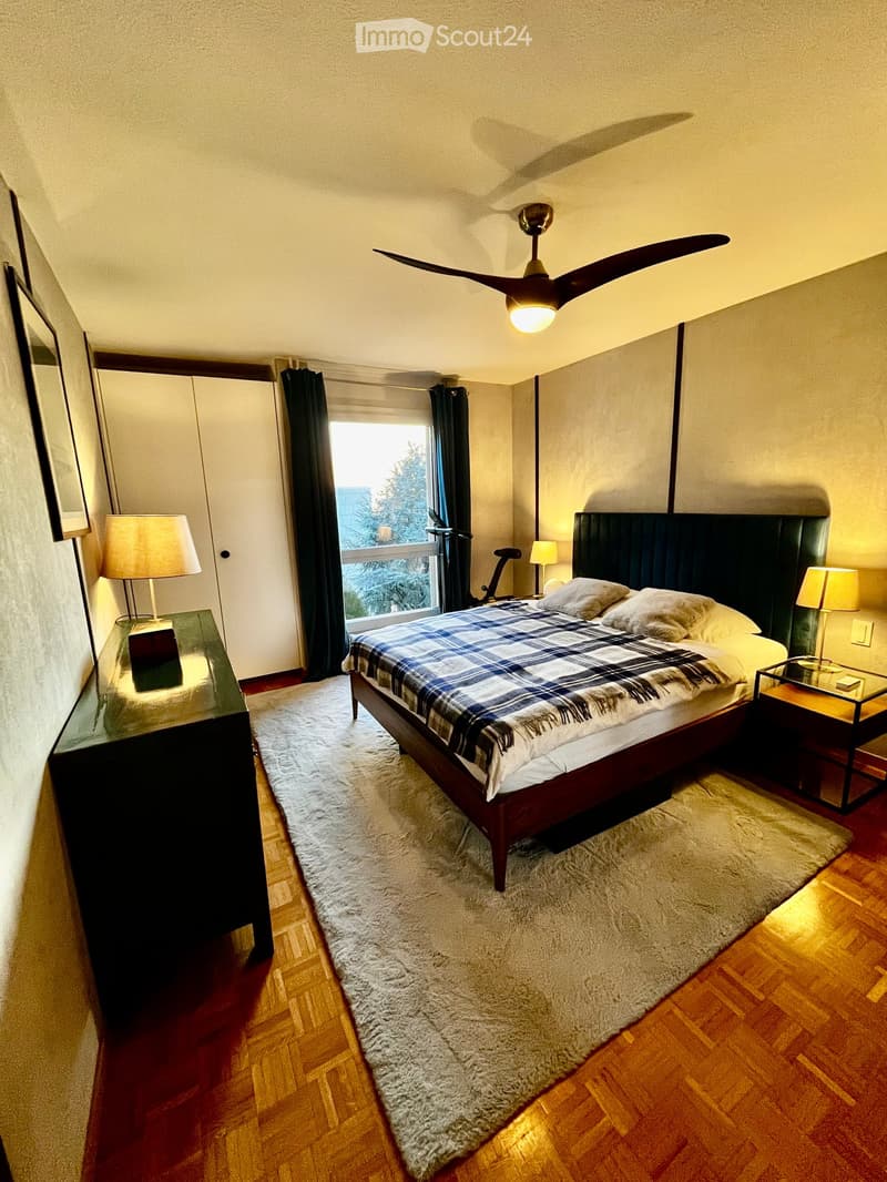 Bedroom. Cozy bedroom with a wooden bed, plaid blanket, nightstands, lamps, and a large window with dark curtains. The room features a wooden floor and a soft white rug.