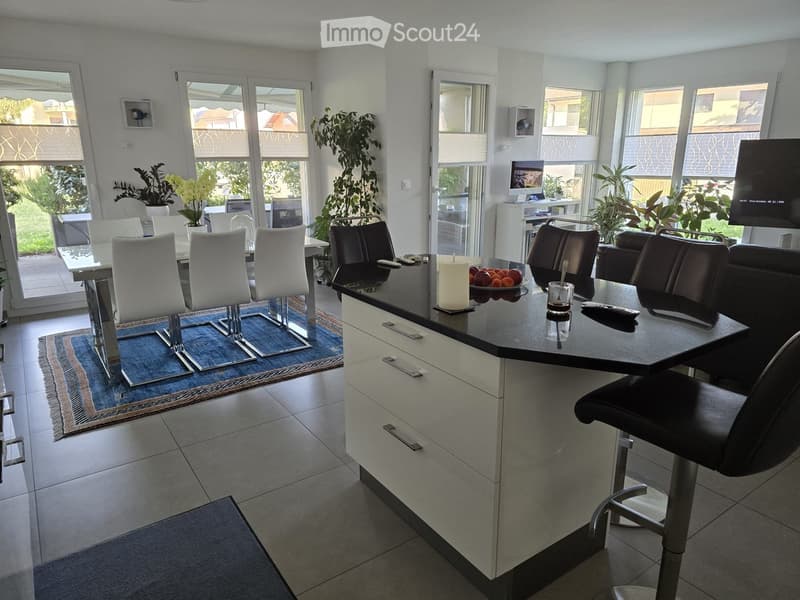 Modern kitchen with island, chairs, table, candle, fruit bowl, and screen.