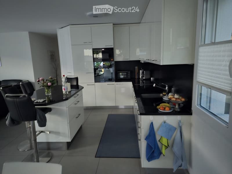 Modern kitchen with white cabinets, black countertops, and stainless steel appliances. Includes a sink, microwave, oven, and a small seating area with stools.