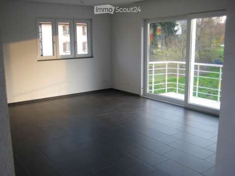 Empty room with dark tiled floor, white walls, large sliding glass door leading to a balcony with metal railing.