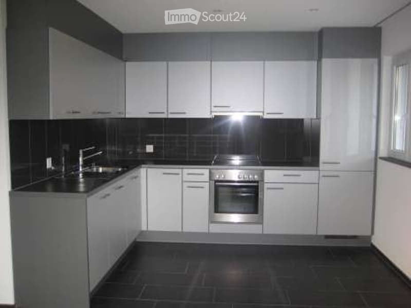 Modern kitchen with white cabinets, black tiled backsplash, stainless steel oven, and sink.