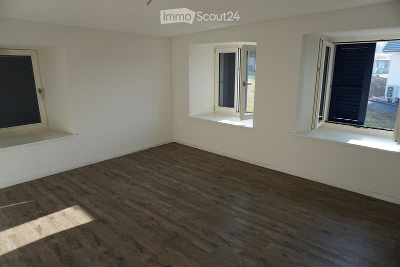 Empty room with wooden flooring and white walls, featuring three windows with shutters and a small built-in shelf beneath one window.