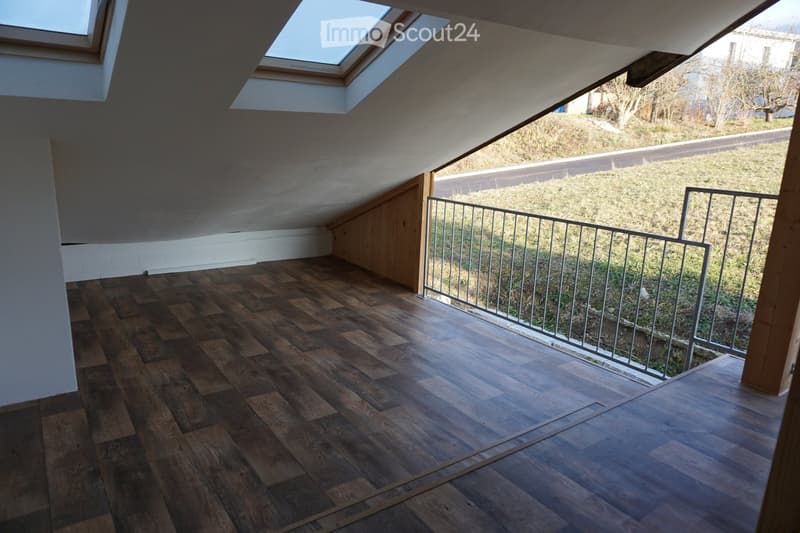 Empty attic space with wooden flooring, skylight windows, and a metal railing leading to an outdoor area.