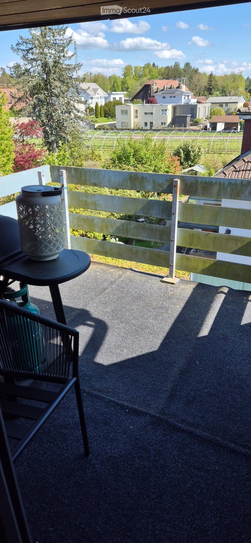 Balcony with a view of a green landscape, featuring a chair, a small table, and a decorative candle holder.