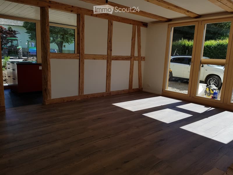 Empty room with wooden flooring, large windows, and exposed wooden beams on the ceiling. No furniture or equipment is present.