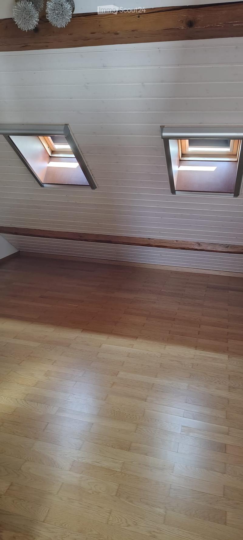 Completely empty room with wooden flooring and white paneled walls. Two skylights provide natural light.