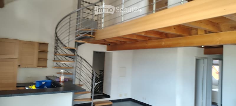Open-plan space with a modern spiral staircase leading to an upper level, featuring a countertop, cabinet, and stool.