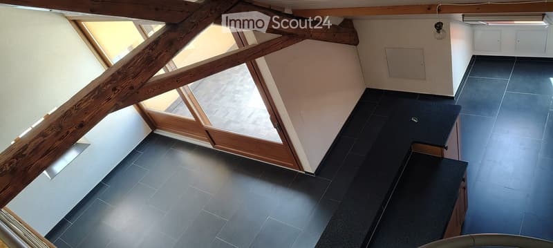 Empty room with dark tiled floor, exposed wooden beams, and large windows allowing natural light. No furniture or equipment present.