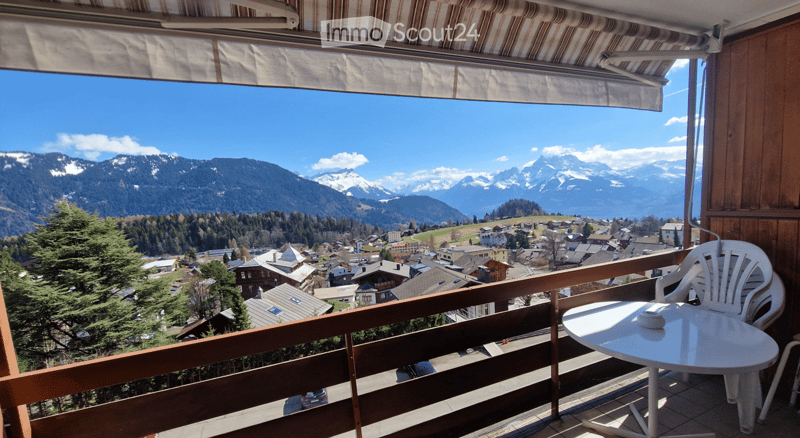 balcony with table and chairs, wooden railing, view of mountains and village