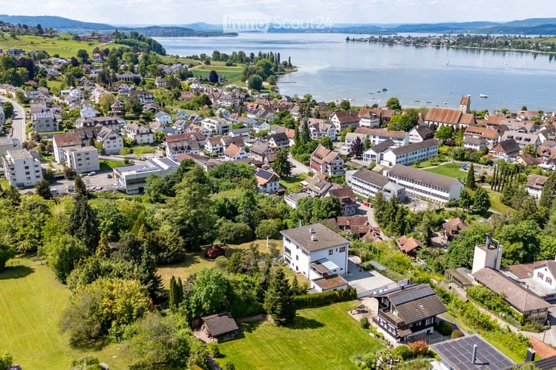 Aerial view of a town with numerous houses, green spaces, and a lake in the background.