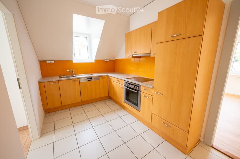 Modern kitchen with light wooden cabinets, white tiled floor, granite countertops, and stainless steel appliances including a sink, dishwasher, and oven. The backsplash is orange tiles, and there is a window above the sink.