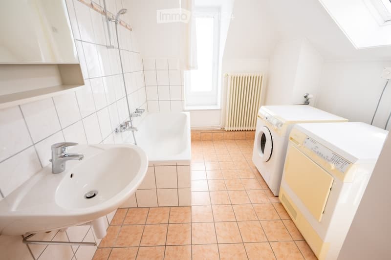 Bright bathroom with a sink, bathtub, washing machine, and dishwasher. Light-colored tiles and a window provide natural light.