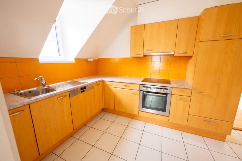 Modern kitchen with light wooden cabinets, granite countertops, stainless steel sink, dishwasher, and oven. Orange backsplash and white tiled floor.