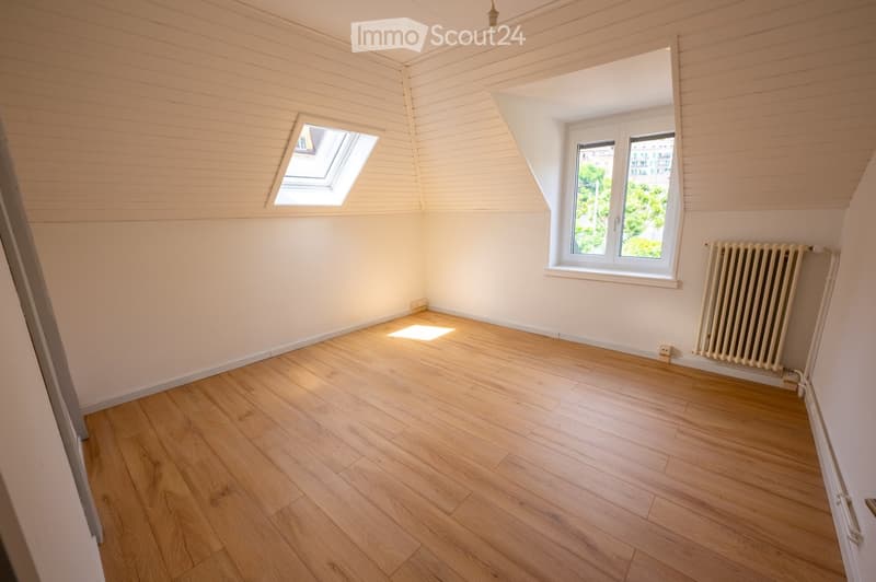 Empty room with wooden flooring, white walls, and large windows, including a skylight and a radiator.
