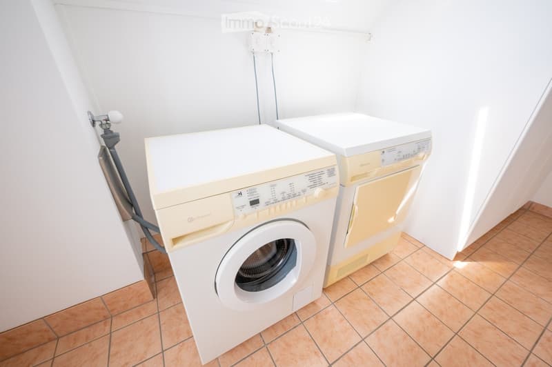 A small bathroom with a washing machine and a dishwasher, both white, placed side by side on a tiled floor.