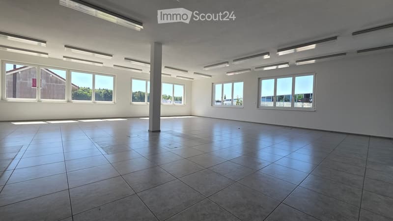 Empty room with tiled floor, white walls, large windows, and a central column. No furniture or equipment present.