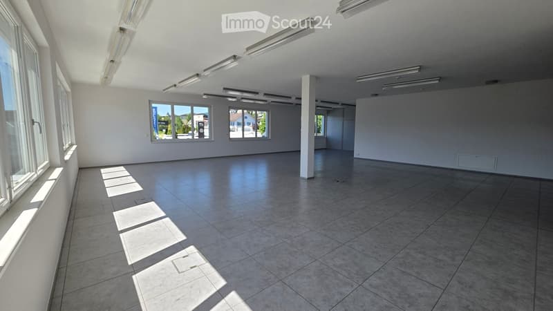 Empty room with tiled floor, white walls, large windows, and fluorescent lighting. No furniture or equipment present.