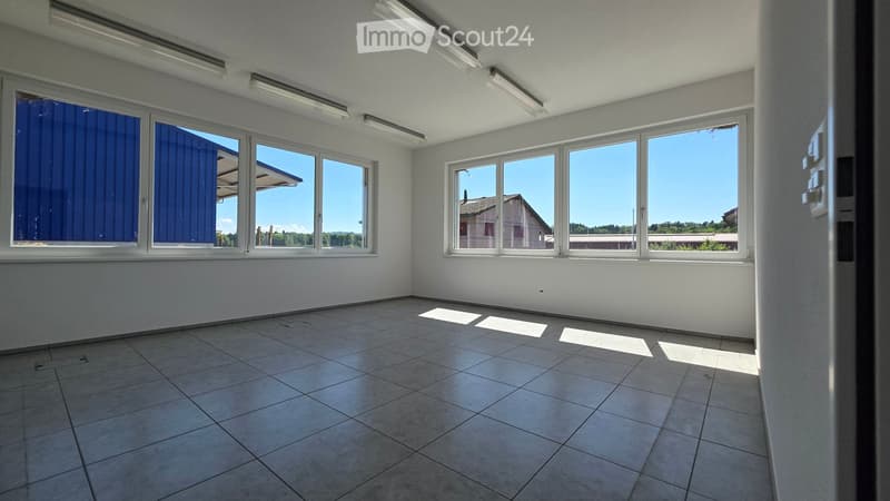 Empty room with tiled floor, white walls, large windows, and fluorescent lighting.