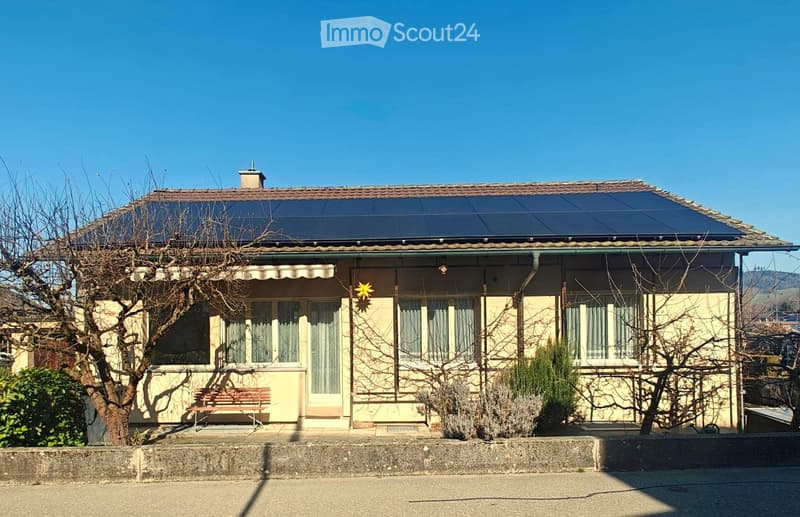 Single-story house with a tiled roof, solar panels, and a bench in front.