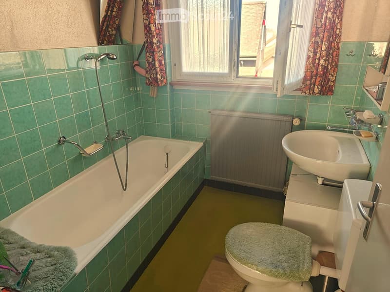 Bathroom with green tiles, bathtub, shower head, sink, toilet, and radiator.