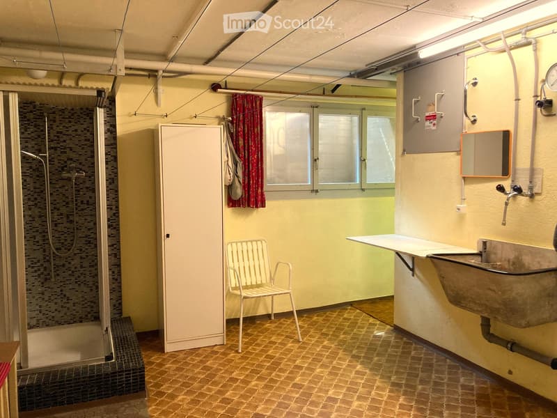 Bathroom with tiled floor, shower area, chair, cabinet, sink, mirror, and pipes. Window provides natural light.