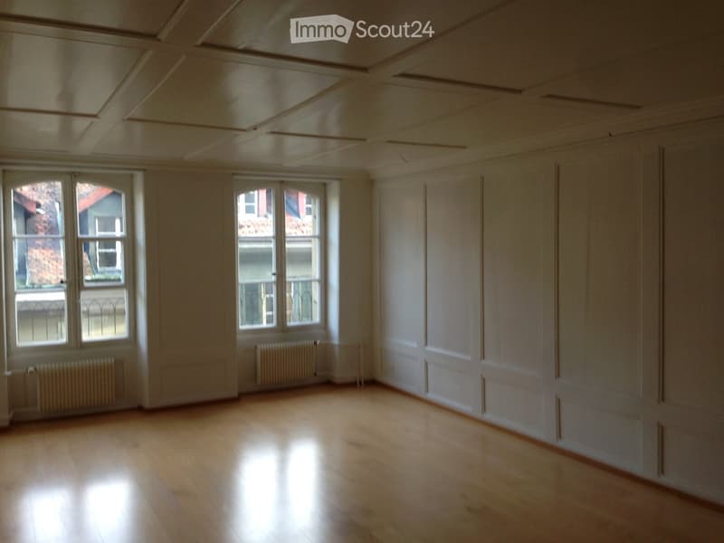 Empty room with wooden flooring, white walls, large windows, and radiators.