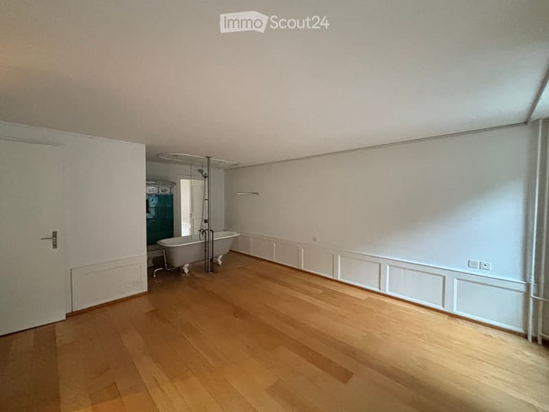 Empty room with wooden flooring, white walls, and a bathtub in the background.