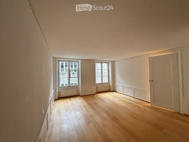 Empty room with wooden flooring, white walls, two windows, and a door. No furniture or equipment present.