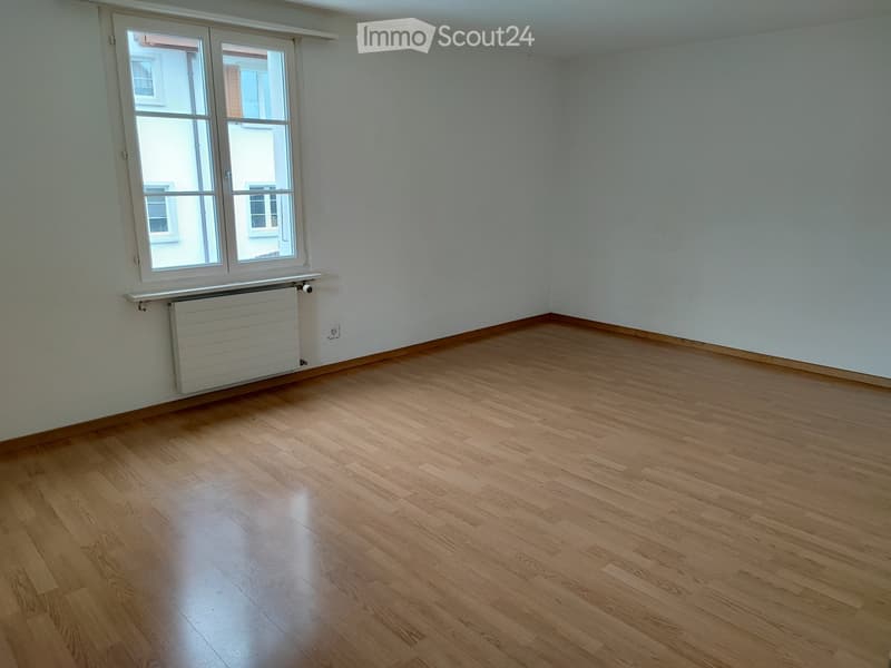 Empty room with wooden flooring, white walls, and a large window with a radiator below it.