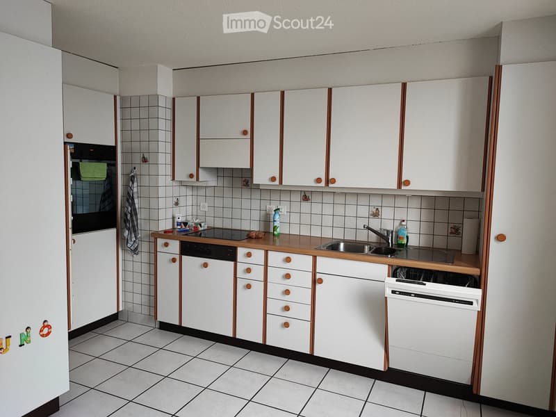 Modern kitchen with white cabinets, wooden countertop, sink, dishwasher, and oven. The walls are tiled with decorative tiles, and the floor is tiled as well.