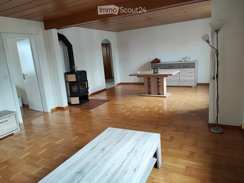 Bright living room with wooden flooring, fireplace, sofa, dining table, and floor lamp.