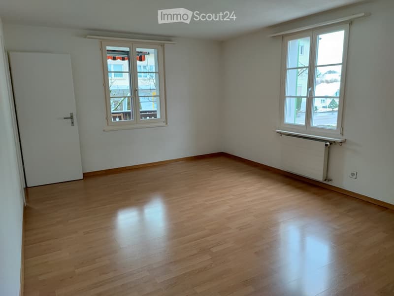 Empty room with wooden flooring, white walls, two windows, and a radiator. No furniture or equipment present.