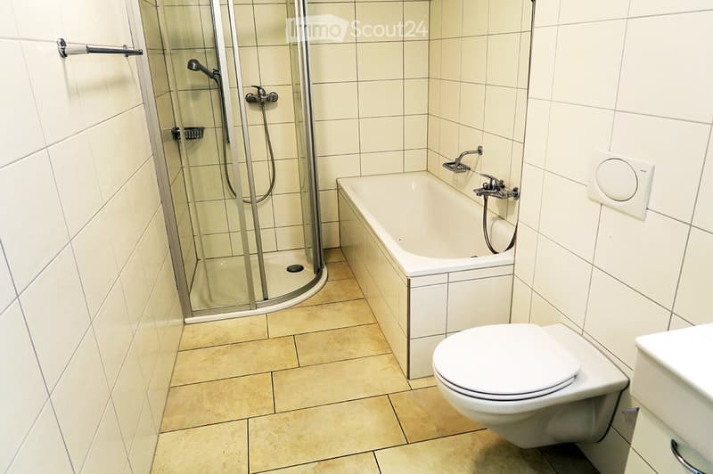 Modern bathroom with a bathtub, toilet, and glass-enclosed shower stall. Light-colored tiles and a sleek design.