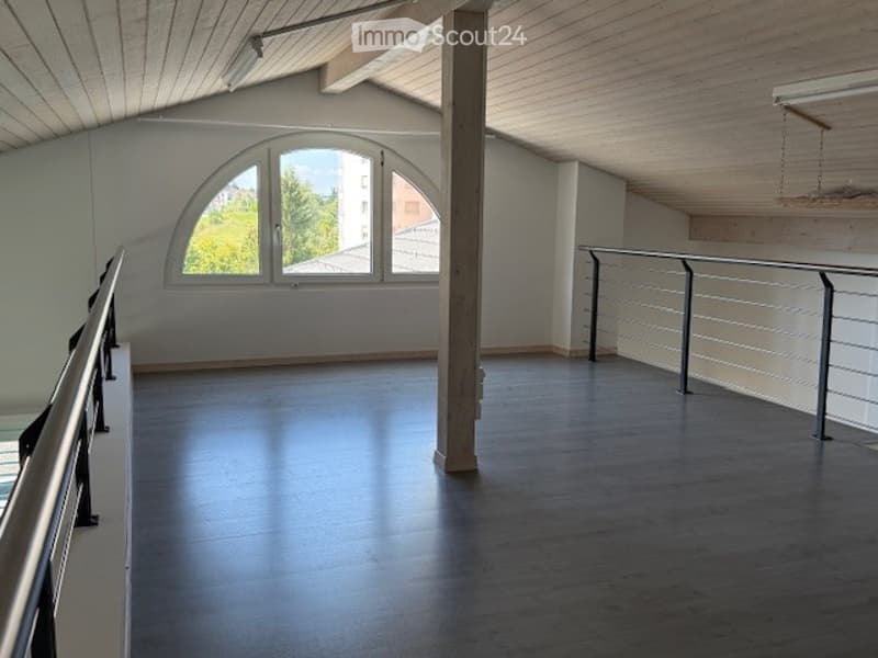 Empty attic space with wooden floors, white walls, large arched windows, and metal railings.