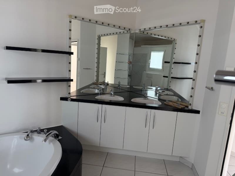 Modern bathroom with white tiled walls, a large mirrored vanity with double sinks, sleek black countertops, and a bathtub. The space features built-in cabinets and modern fixtures.