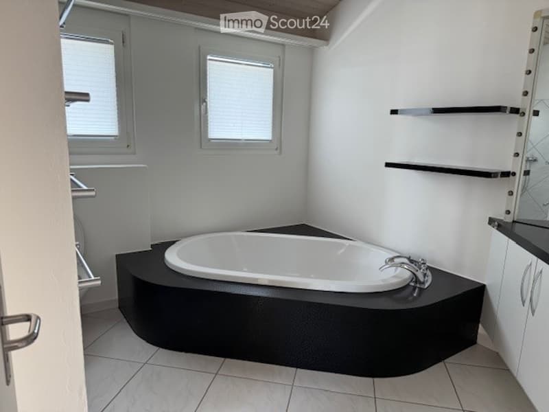 Modern bathroom with a corner bathtub, sleek black surround, white tiled floor, and built-in black shelves.