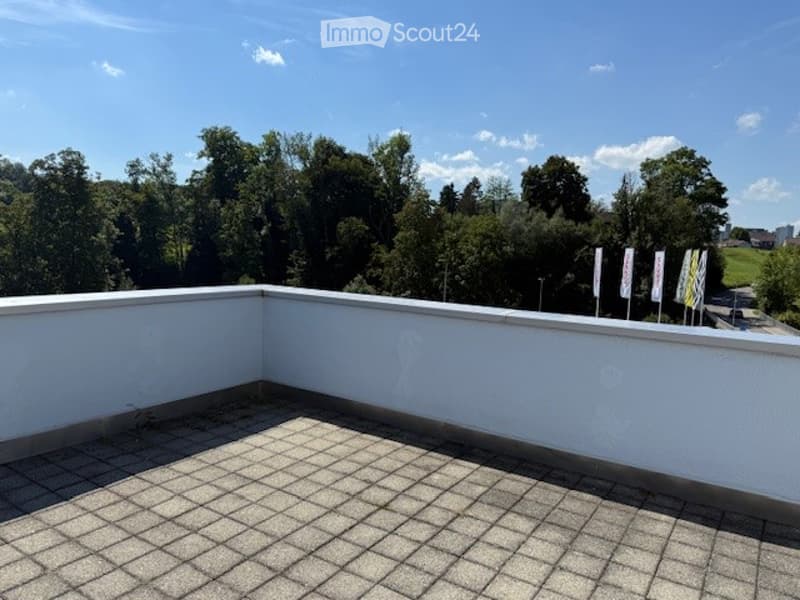 Roof terrace with tiled flooring, white walls, and a scenic view of a green, wooded area with trees and distant structures.
