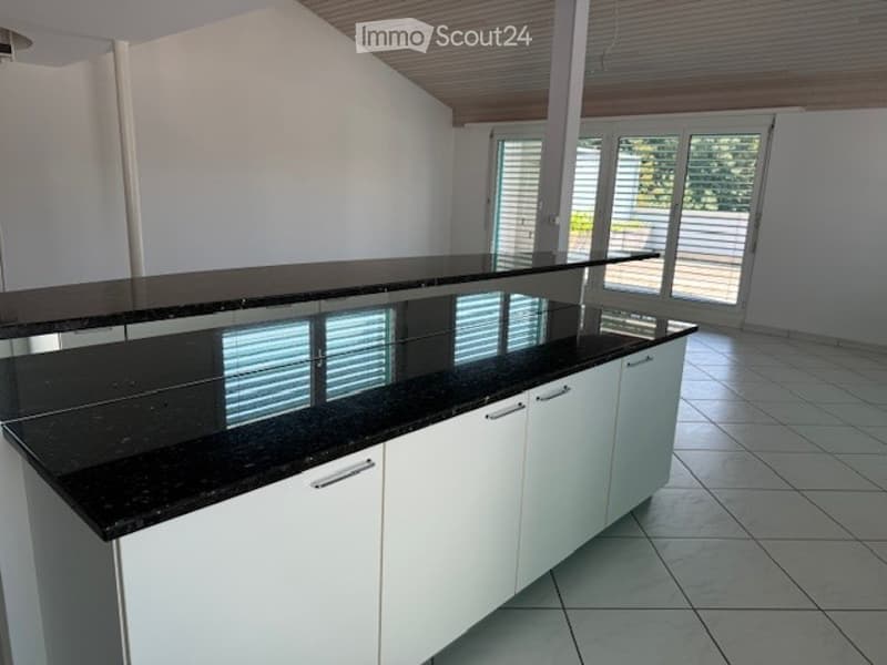Modern kitchen with white cabinets, black granite island, large windows, and tiled floor.